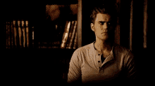 a man in a gray shirt is sitting in front of a bookshelf .