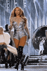 a woman is standing on a stage wearing thigh high boots and a silver dress .