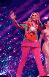 a woman in a pink suit is waving at the camera