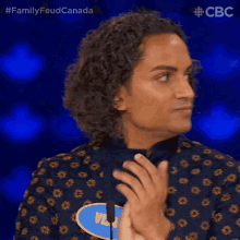 a man with curly hair is standing in front of a microphone on a show called family feud canada .