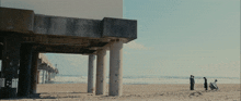 people standing under a pier on a beach