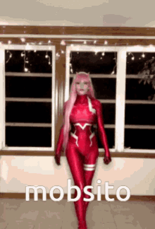 a woman in a red superhero costume is standing in front of a window with the word mobsito written on the bottom .