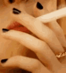 a close up of a woman smoking a cigarette with black nail polish .