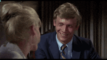 a man in a suit and tie smiles next to a woman in a bun