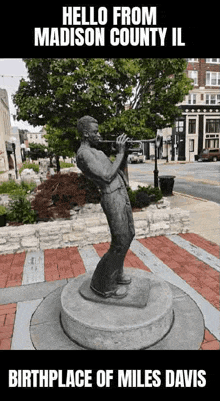 a statue of a man playing a trumpet with the words hello from madison county il birthplace of miles davis below it