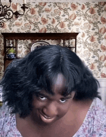 a woman with black hair is making a funny face in front of a floral wallpaper