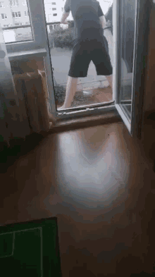 a man in black shorts is standing on a balcony looking out a window .