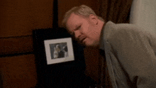 a man in a suit is looking at a framed picture of a man and woman kissing .