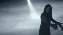 a woman in a black dress is standing in a dark room holding a sword .