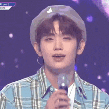 a young man wearing a plaid shirt and a hat is holding a microphone .