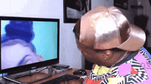 a man wearing a hat is looking at a computer monitor