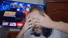 a man covering his face in front of a tv screen that says sonic racing cross worlds