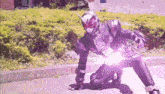 a man in a superhero costume is kneeling down on the sidewalk with a purple light coming out of his hand .