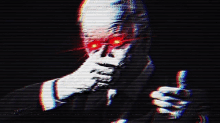 a man in a suit is covering his face with his hand while giving a thumbs up .