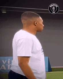 a man in a white shirt stands on a field with a logo that says mbappe live