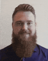a man with a beard wearing a blue shirt smiles for the camera