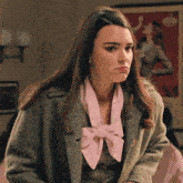 a woman wearing a green coat and a pink scarf looks at the camera