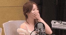 a woman is laughing in front of a microphone while covering her mouth with her hand .