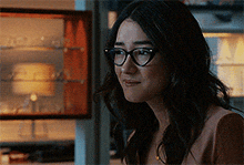 a woman wearing glasses is standing in front of a glass display case .