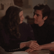 a man and a woman are holding hands and looking at each other while sitting at a table .