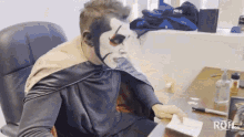 a man with face paint is sitting at a desk in front of a sign that says rq4.com