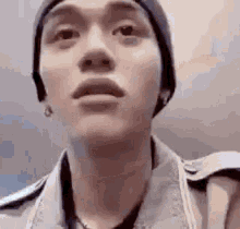 a man wearing a beanie and a denim jacket is looking up at the camera .
