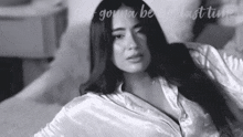 a black and white photo of a woman in a satin robe laying on a bed .