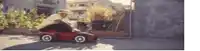 a man is riding a red toy car on a street .