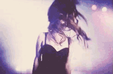 a woman in a black dress is dancing on a stage with her hair blowing in the wind .