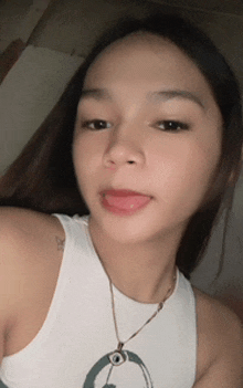 a woman wearing a white tank top and a necklace is sticking out her tongue