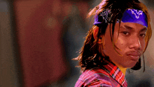 a man wearing a purple bandana and a plaid shirt looks at the camera