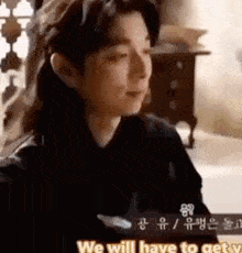 a man in a black shirt is sitting in a room talking to someone .