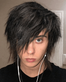 a young man wearing headphones and a chain around his neck looks at the camera