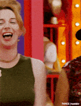 a woman in a green tank top is laughing with her mouth wide open