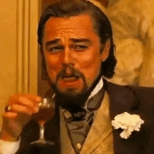 a man with a beard is drinking a glass of wine .