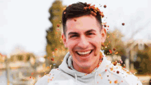 a man in a white hoodie is smiling with confetti falling on his face
