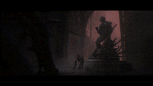 a statue of a man holding a sword in a dark room with a red background .