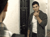 a man in a hoodie is standing in front of a door and looking at himself in the mirror .