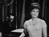 a black and white photo of a woman singing while a man plays the piano