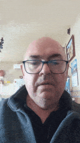 a bald man wearing glasses and a black shirt looks at the camera