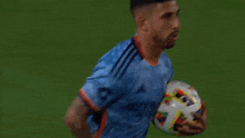 a soccer player in a blue jersey is holding a soccer ball in his hands .