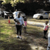 a group of people are walking down a dirt road with cars parked behind them