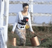 a woman is carrying two buckets and a shovel in a field .