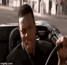 a man in a suit and tie is sitting in a car holding the steering wheel .