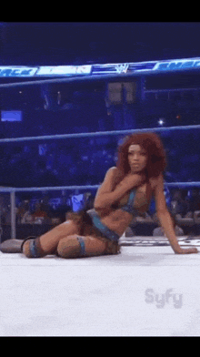 a woman is kneeling on the ground in a wrestling ring with syfy in the corner