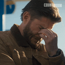 a man in a brown jacket is covering his face with his hand and the word countdown is on the bottom right