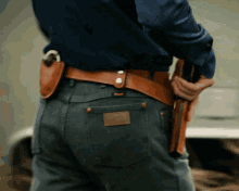 a man wearing a blue shirt and a brown leather belt holds a gun