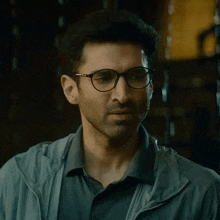 a man wearing glasses and a grey jacket looks to the side