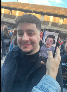a man holds up a cell phone with a picture of him on it