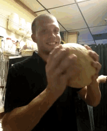 a man in a black shirt is smiling while holding a large melon in his hands